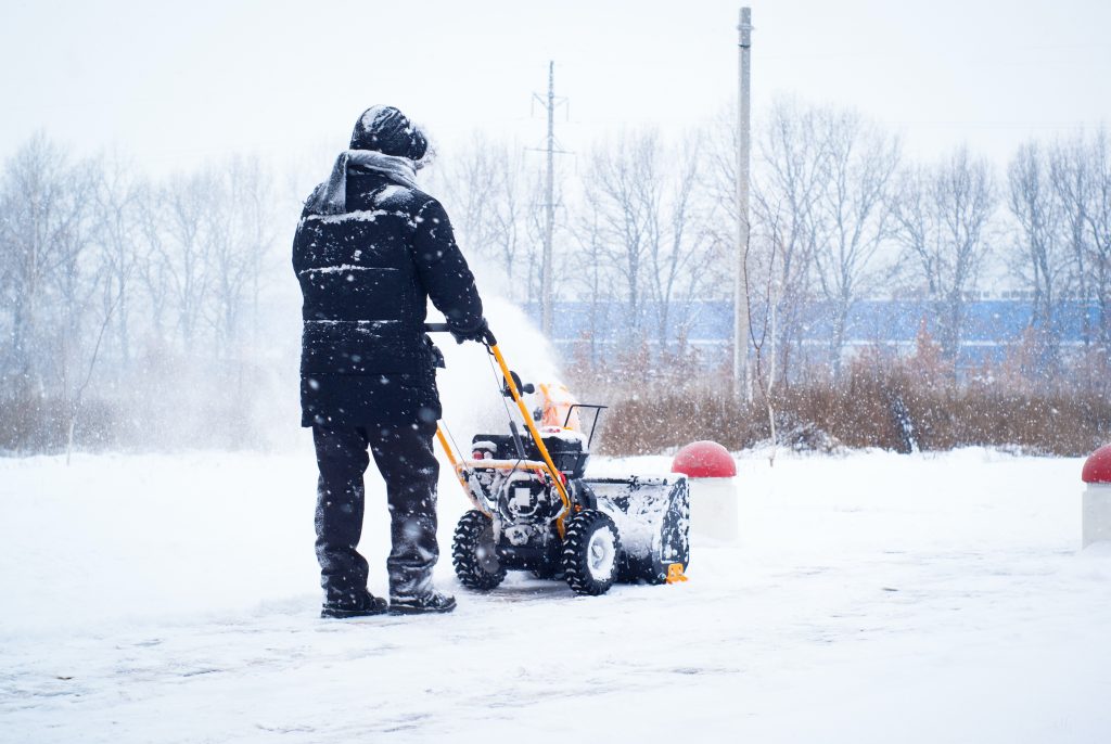 A man cleans snow from sidewalks with snowblower.